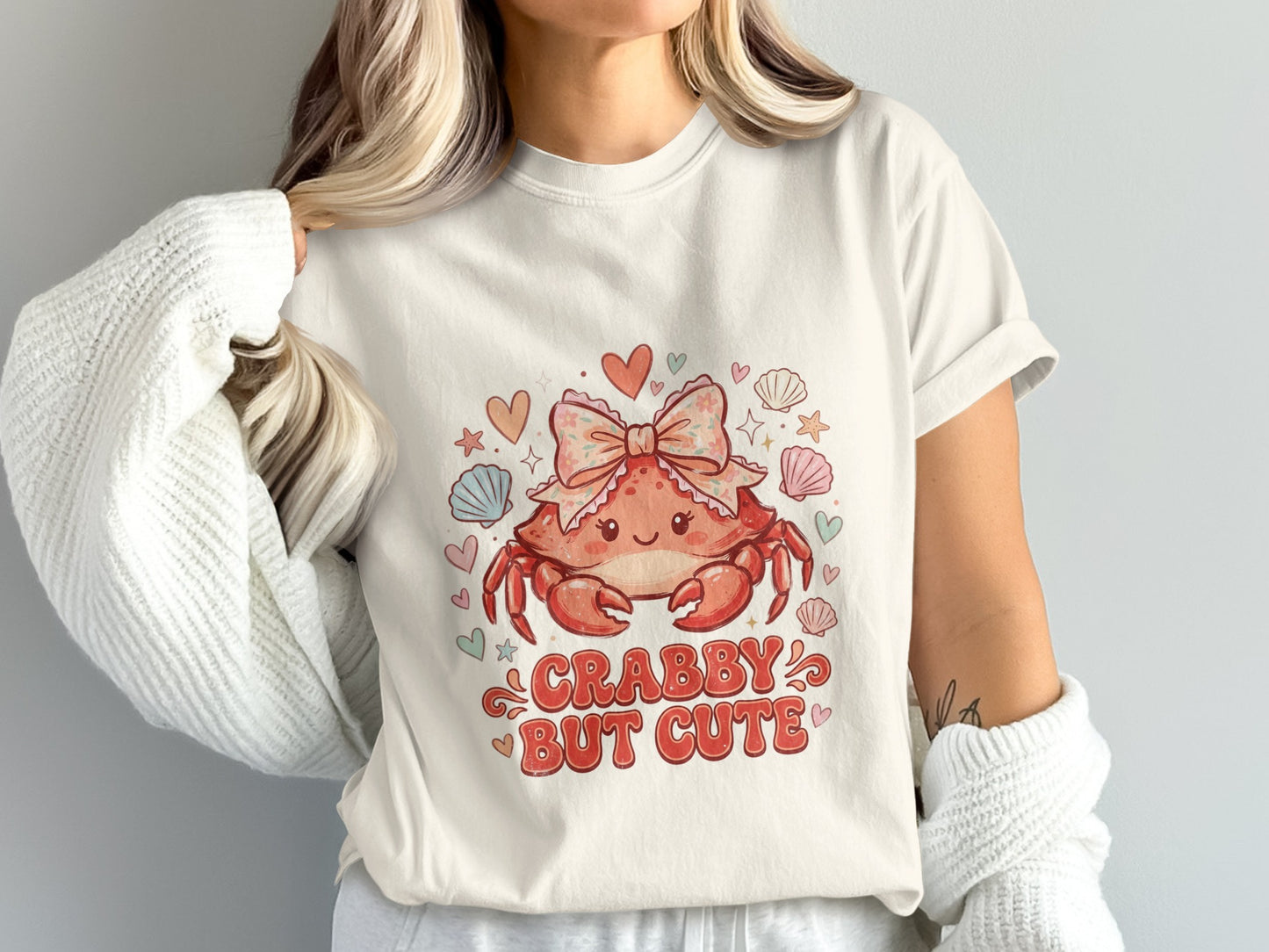 Cream t-shirt with a cartoon crab wearing a pink bow and the text "CRABBY BUT CUTE".