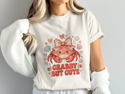 Cream t-shirt with a cartoon crab wearing a pink bow and the text "CRABBY BUT CUTE".
