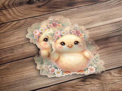 Two fluffy yellow chicks wearing floral wreaths on a wooden surface.