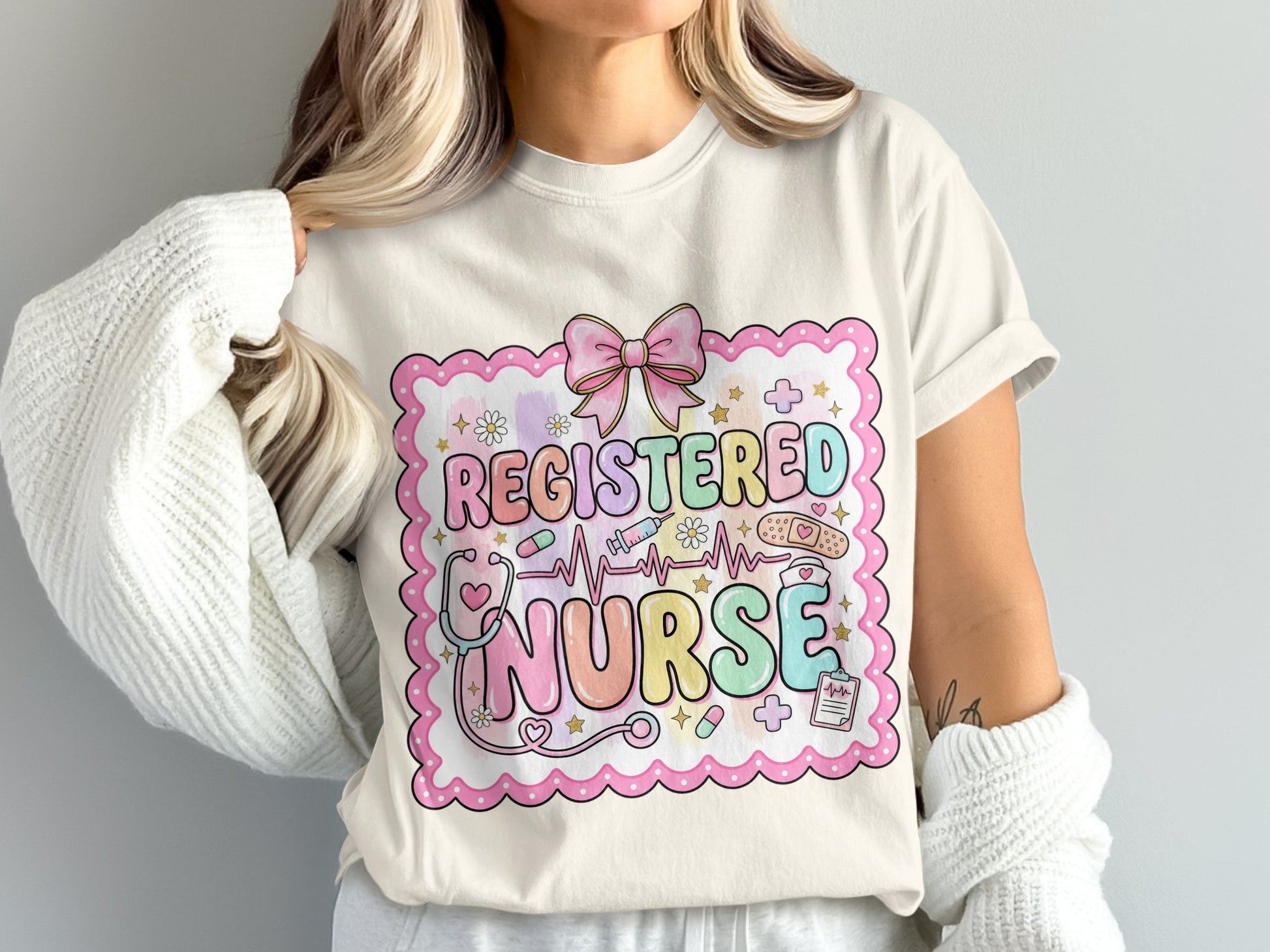 Registered Nurse text with medical icons and pink bow on cream t-shirt.