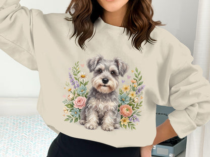 Gray schnauzer puppy surrounded by flowers on a cream sweatshirt.