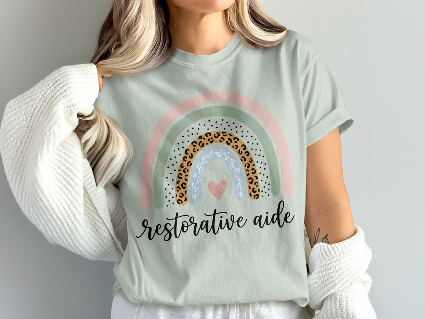 Light green t-shirt with rainbow graphic and "restorative aide" text.