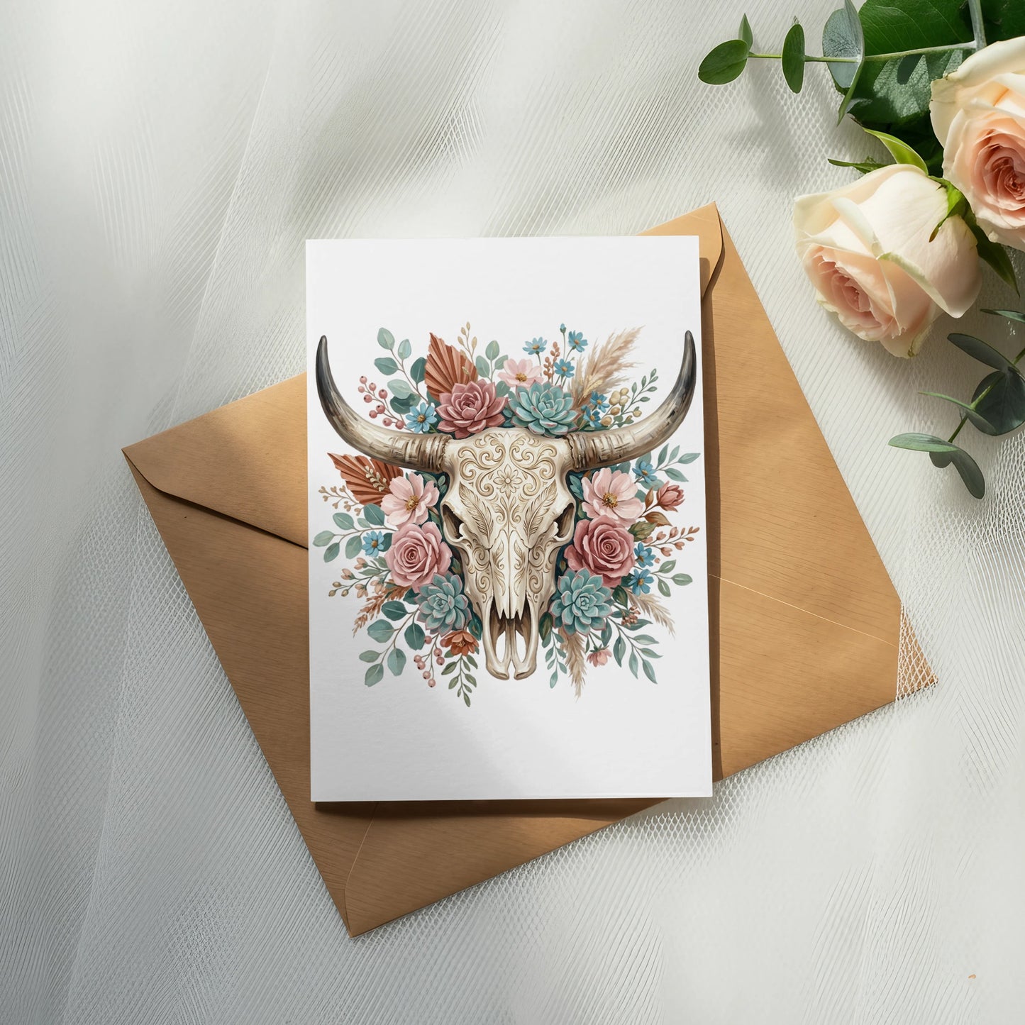 Card with floral decorated bull skull on an envelope, with roses nearby.