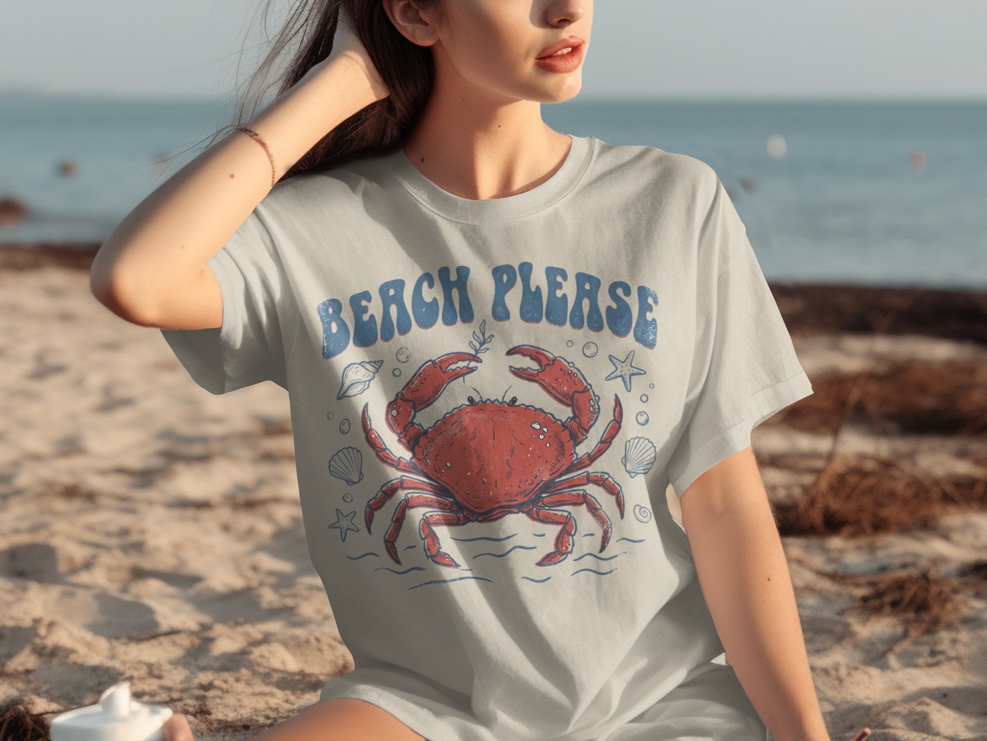 Woman wearing a gray t-shirt with a blue crab and "Beach Please" graphic.