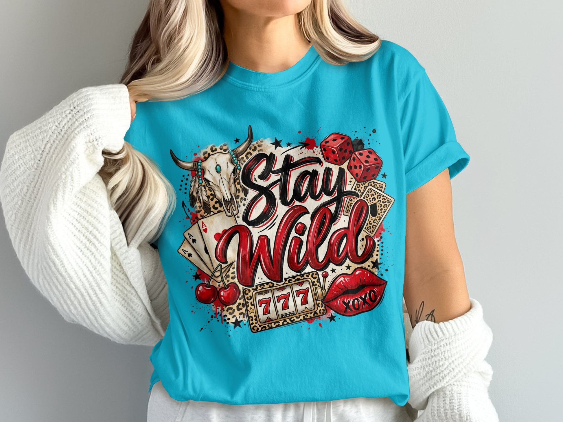 "Stay Wild" text with bull skull, dice, cards, cherries, and lips graphic on blue t-shirt.