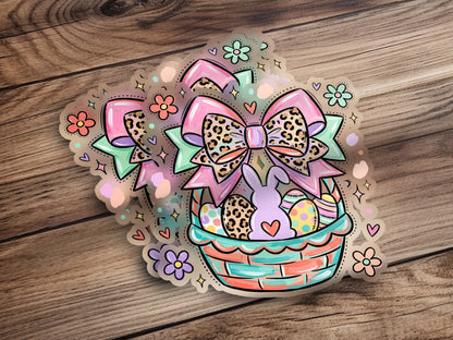 Easter basket with bow, bunny, eggs, and flowers on a wooden background.