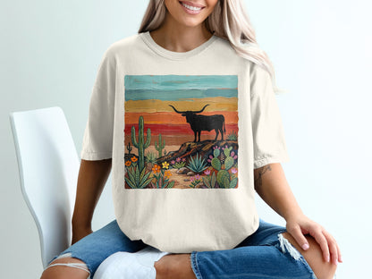 Cream t-shirt with a painted desert landscape featuring a longhorn and colorful sunset.