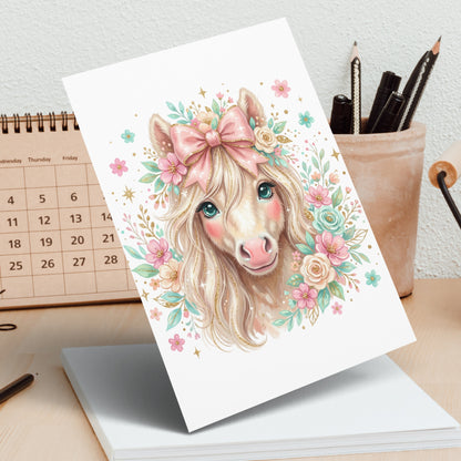 Whimsical unicorn with flowers and pink bow on card, desk background.