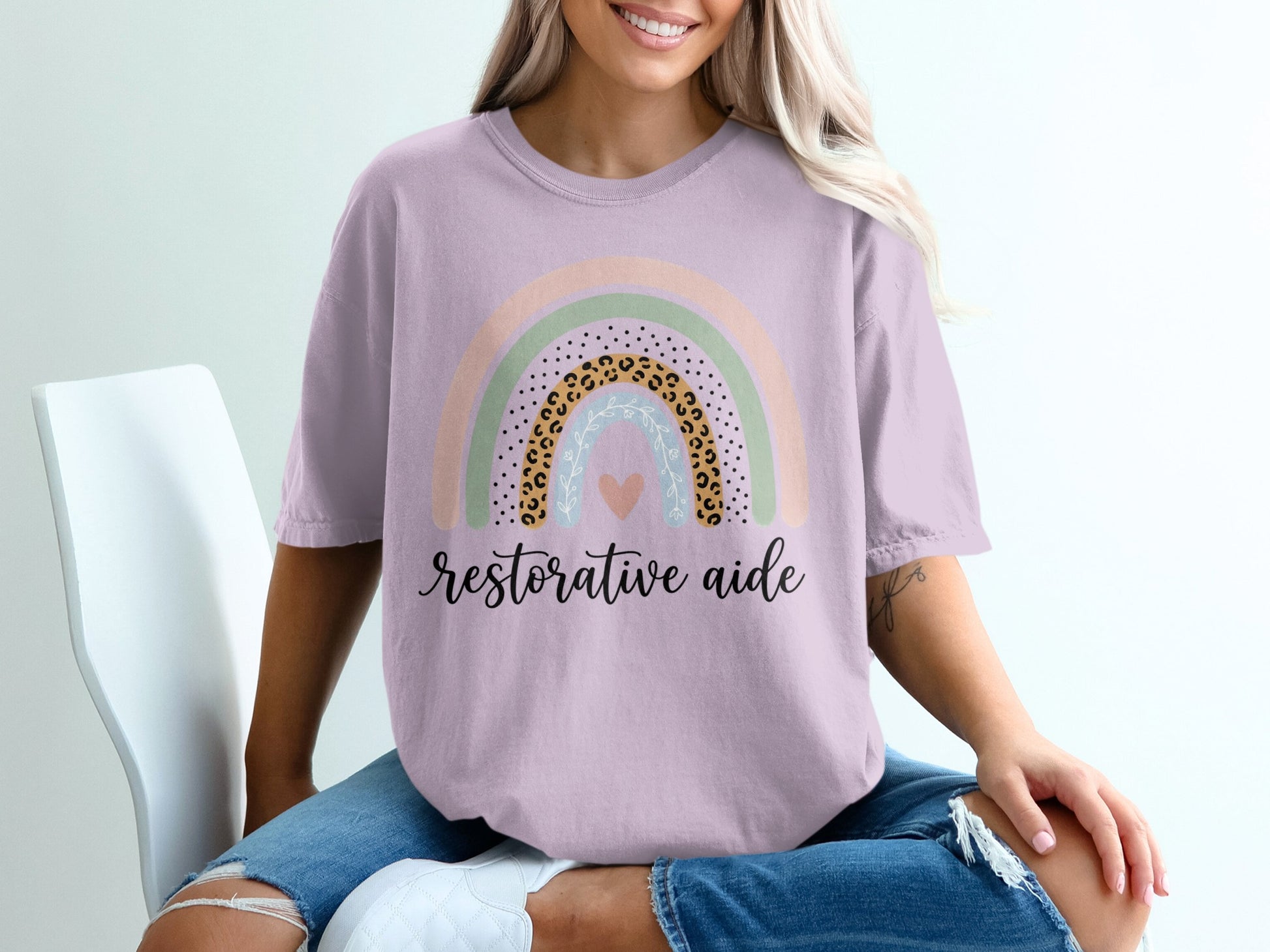 Light purple t-shirt with pastel rainbow graphic and text "restorative aide".