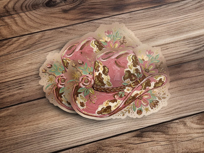 Two pink cowboy hats with floral and gold accents on a wooden background.