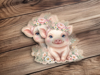 Two cartoon piglets wearing floral crowns sit amongst flowers.