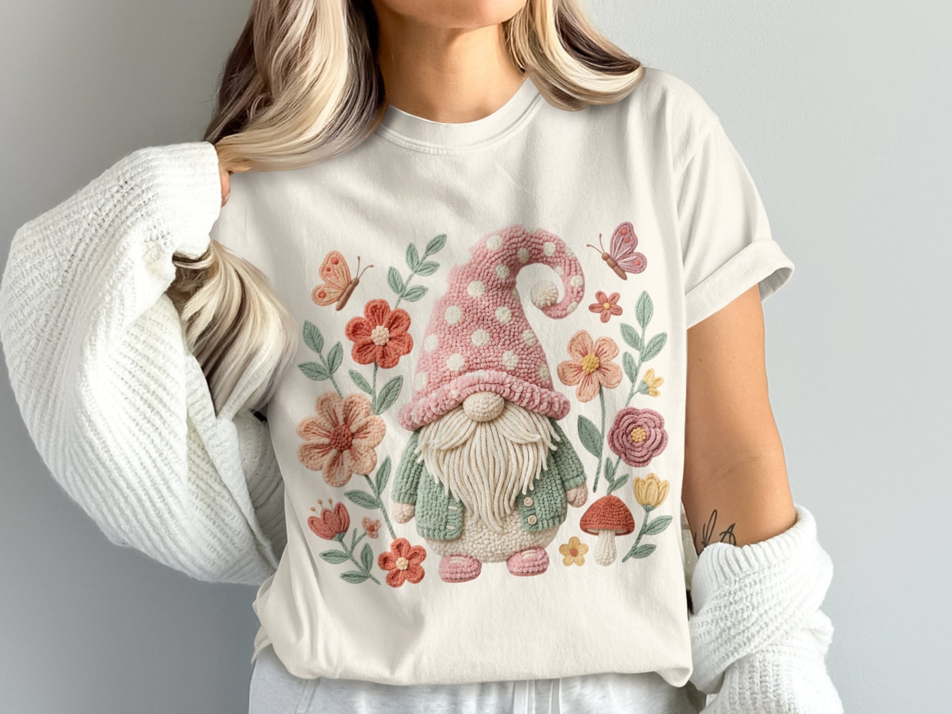 Gnome wearing pink polka dot hat and green sweater surrounded by flowers and butterflies.