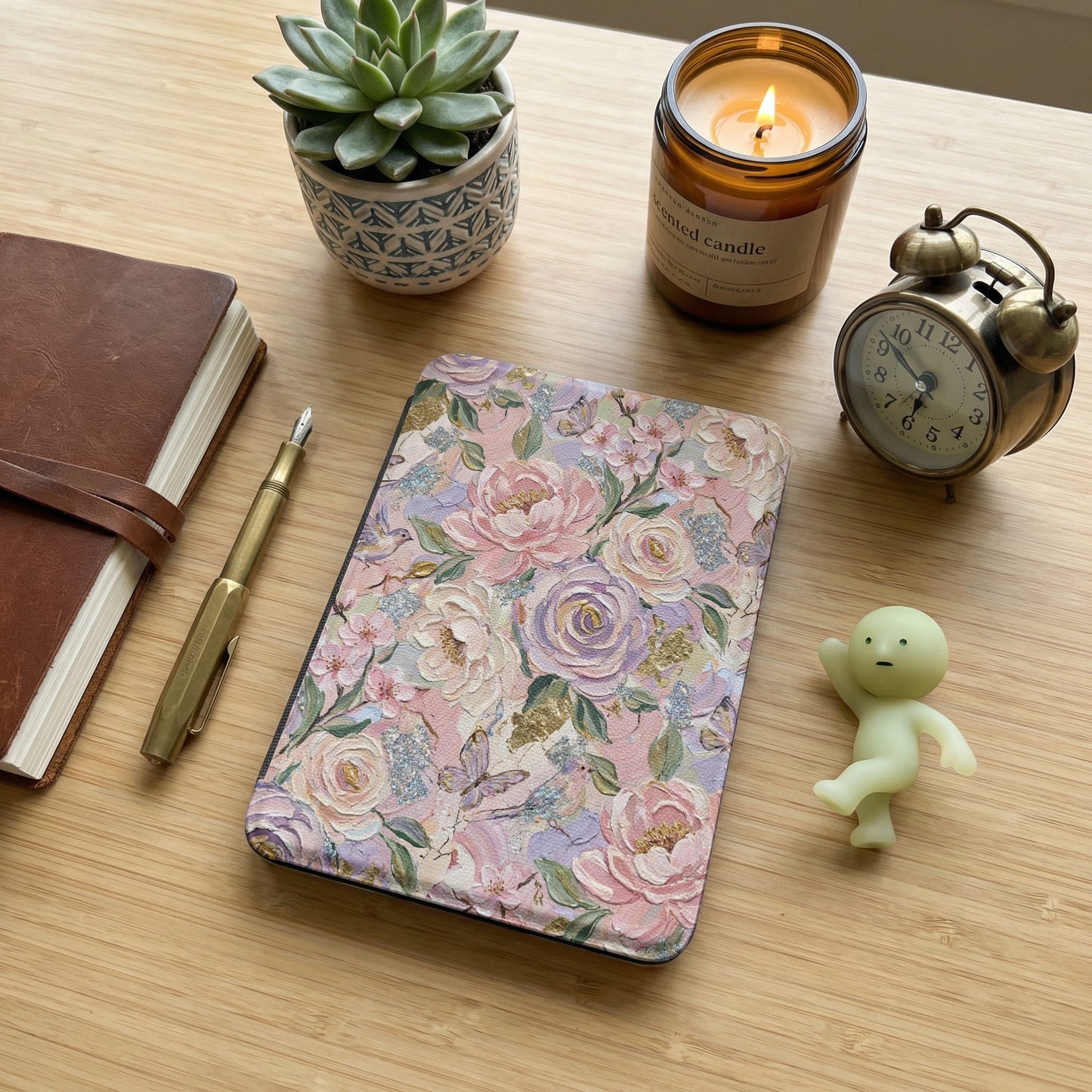 Floral patterned e-reader with a candle, journal, and alarm clock.