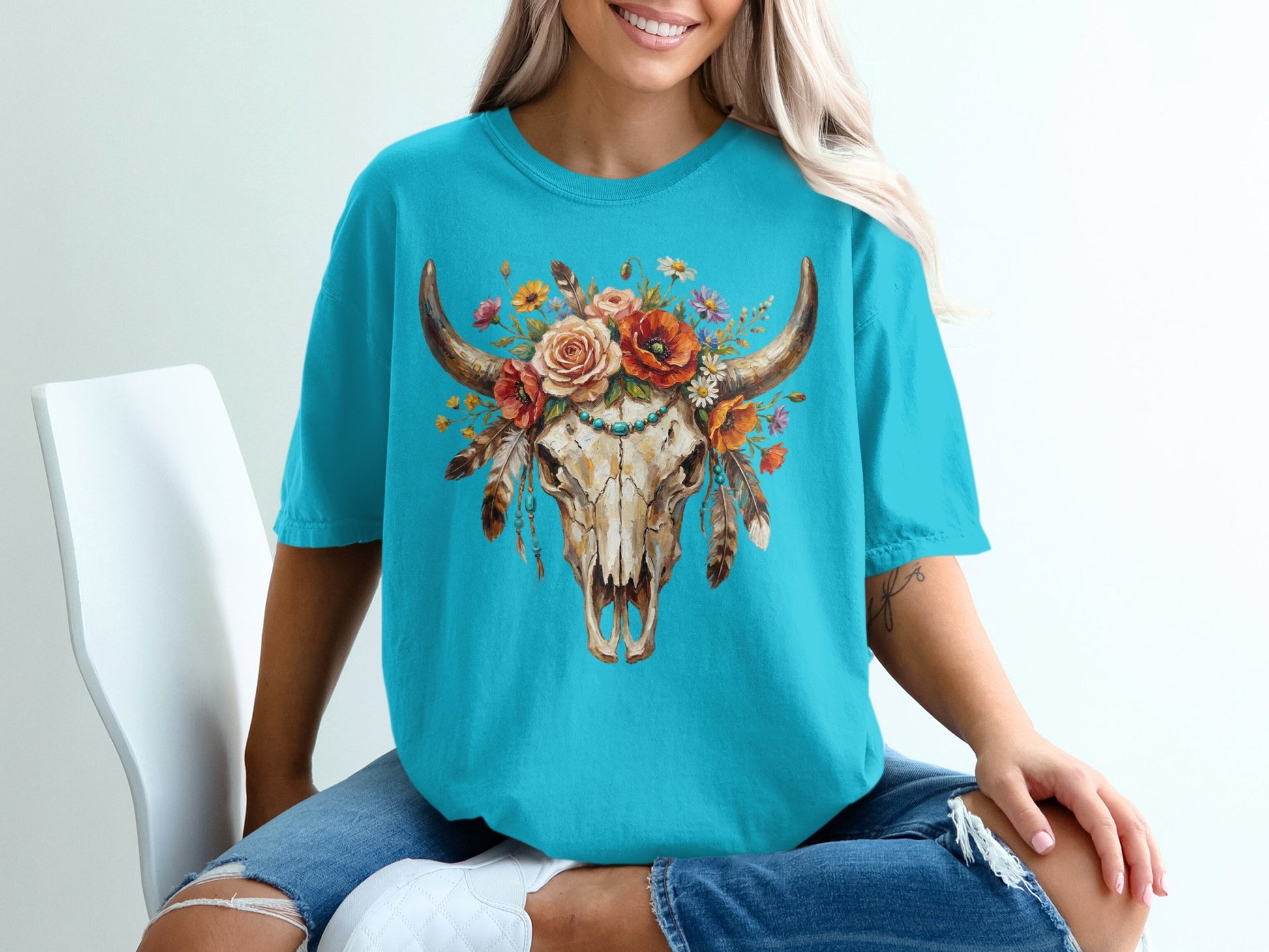 Turquoise t-shirt with a skull adorned with flowers and feathers.