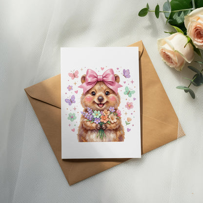 Quokka wearing a pink bow holds a bouquet of flowers on a white card.