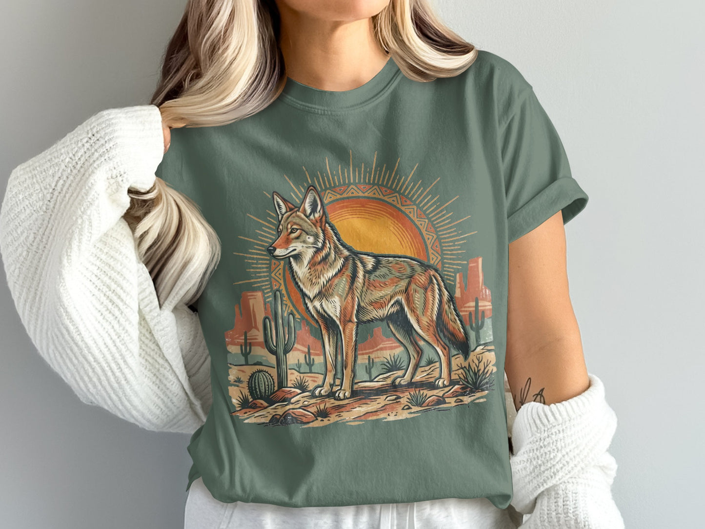 Coyote standing in desert landscape with sun and cacti graphic on green t-shirt.