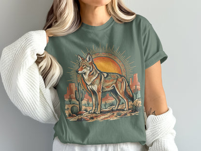Coyote standing in desert landscape with sun and cacti graphic on green t-shirt.