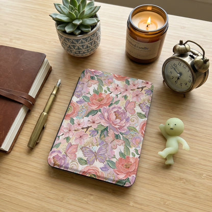 Floral e-reader case with butterflies, next to a journal and alarm clock.