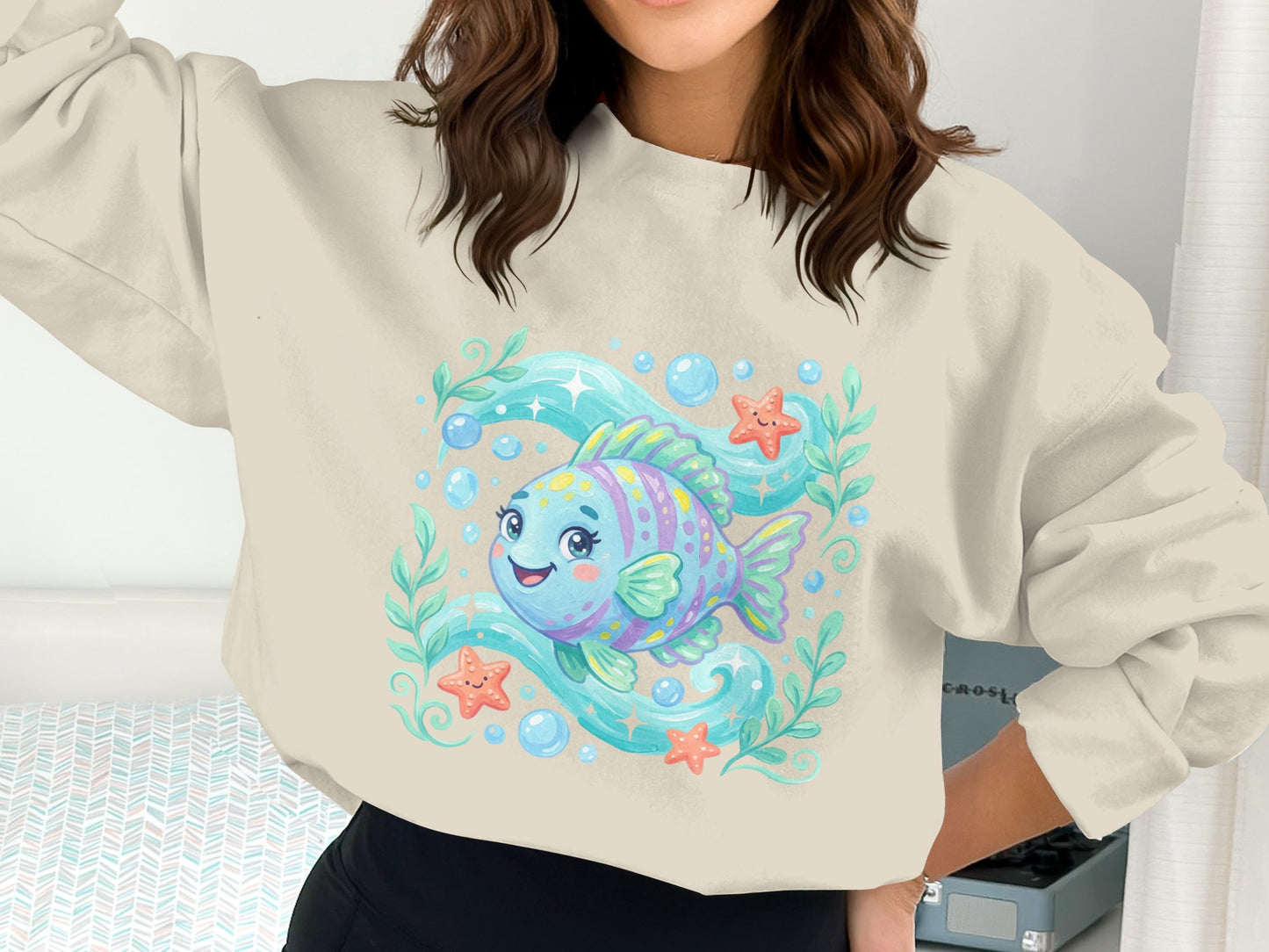 Illustrated smiling fish with bubbles and starfish, on a light cream crewneck sweatshirt.