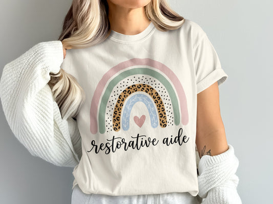 Cream t-shirt with rainbow graphic and text "restorative aide".