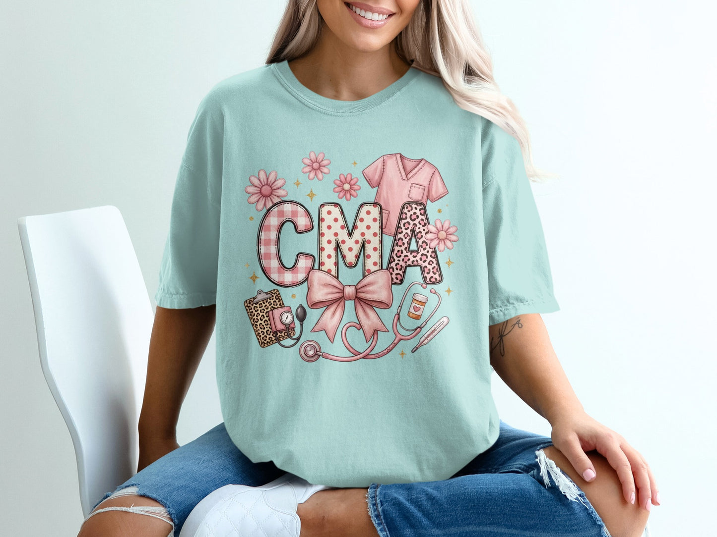 Light blue t-shirt with "CMA" in patterned letters, stethoscope, and scrub top graphic.