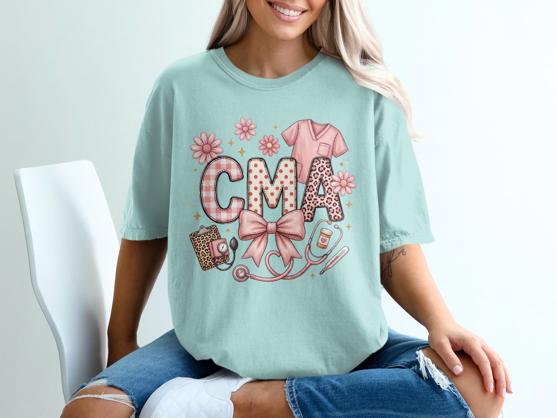 Light blue t-shirt with "CMA" in patterned letters, stethoscope, and scrub top graphic.