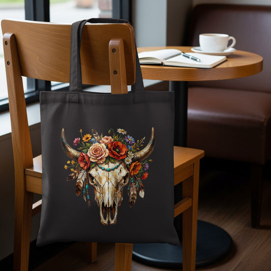 Black tote bag with a steer skull adorned with colorful flowers and feathers.