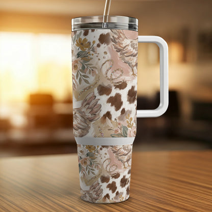 Tumbler with cow print, floral, and feather pattern and a white handle.