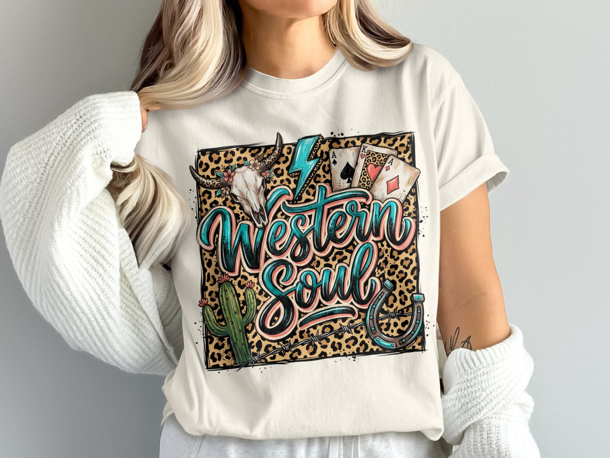 White t-shirt with "Western Soul" in turquoise script, leopard print, cactus, skull, and horseshoe.