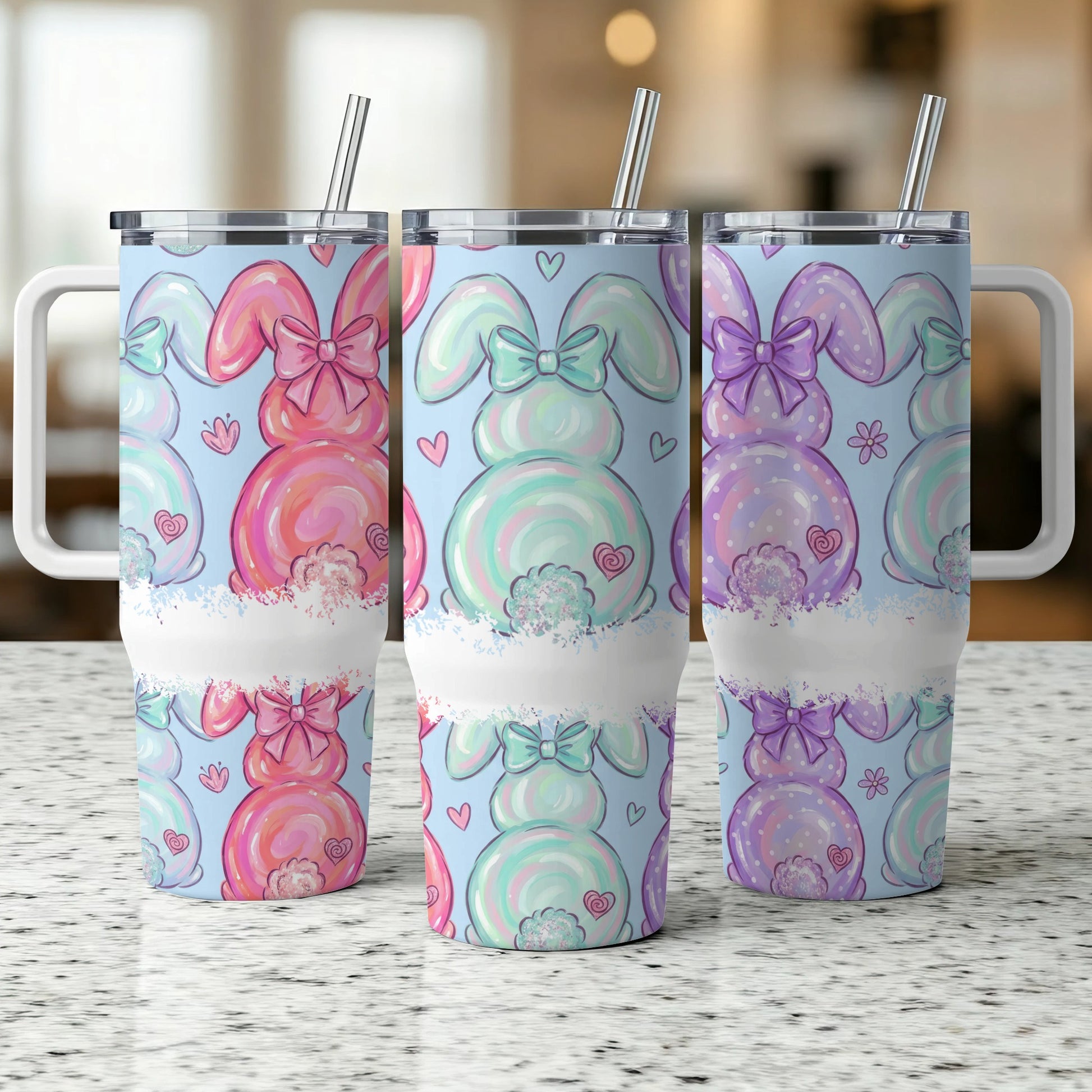 Three pastel bunny tumblers with bows and hearts on a speckled counter.