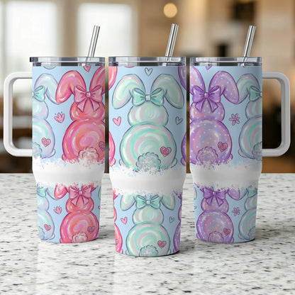 Three pastel bunny tumblers with bows and hearts on a speckled counter.