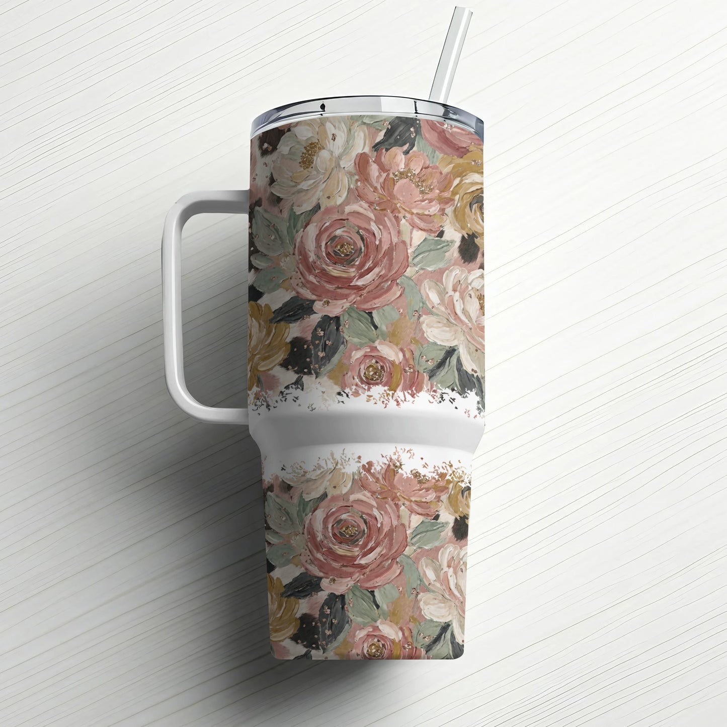 Floral patterned tumbler with handle and straw on white wooden surface.