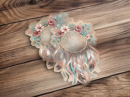 Two dreamcatchers with floral accents and feathers on a wooden background.