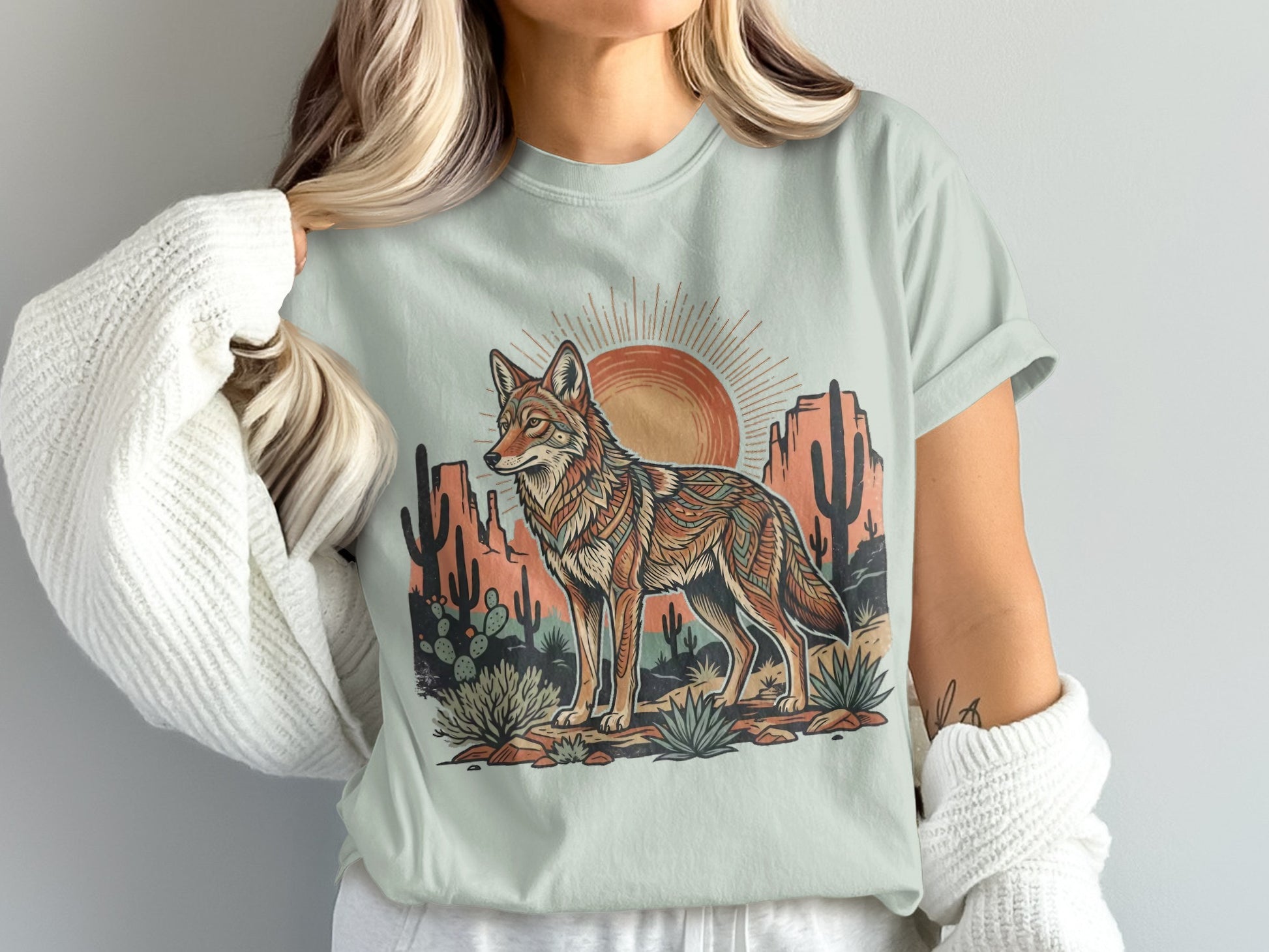 Coyote and desert landscape with sun graphic on a light green t-shirt.