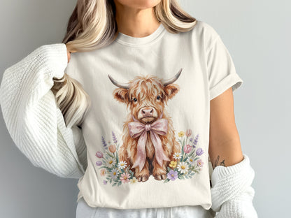 Watercolor highland cow with pink bow surrounded by flowers on cream t-shirt.