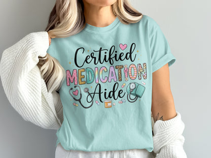 Light blue t-shirt with "Certified Medication Aide" text and medical icons.