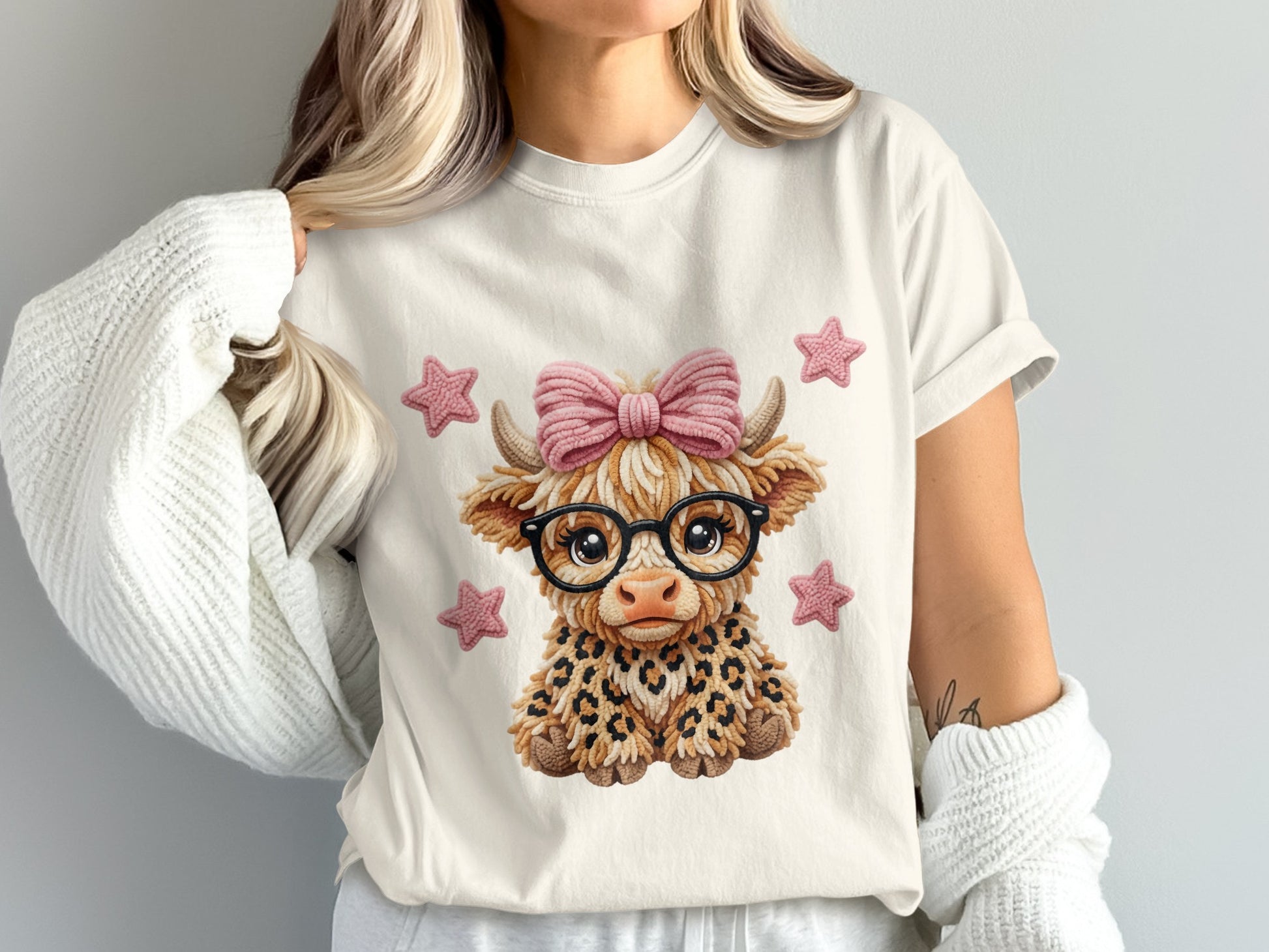 Cartoon Highland cow wearing glasses and a pink bow on a white t-shirt.