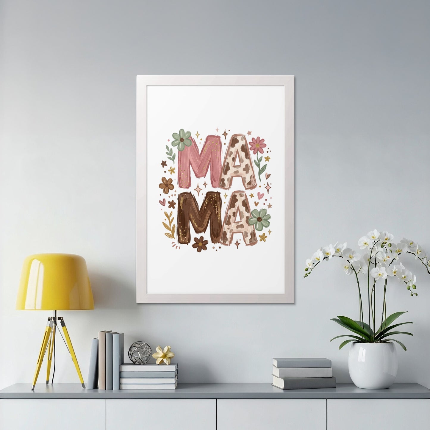 Framed artwork with "MAMA" in floral and cow print, displayed on a shelf.