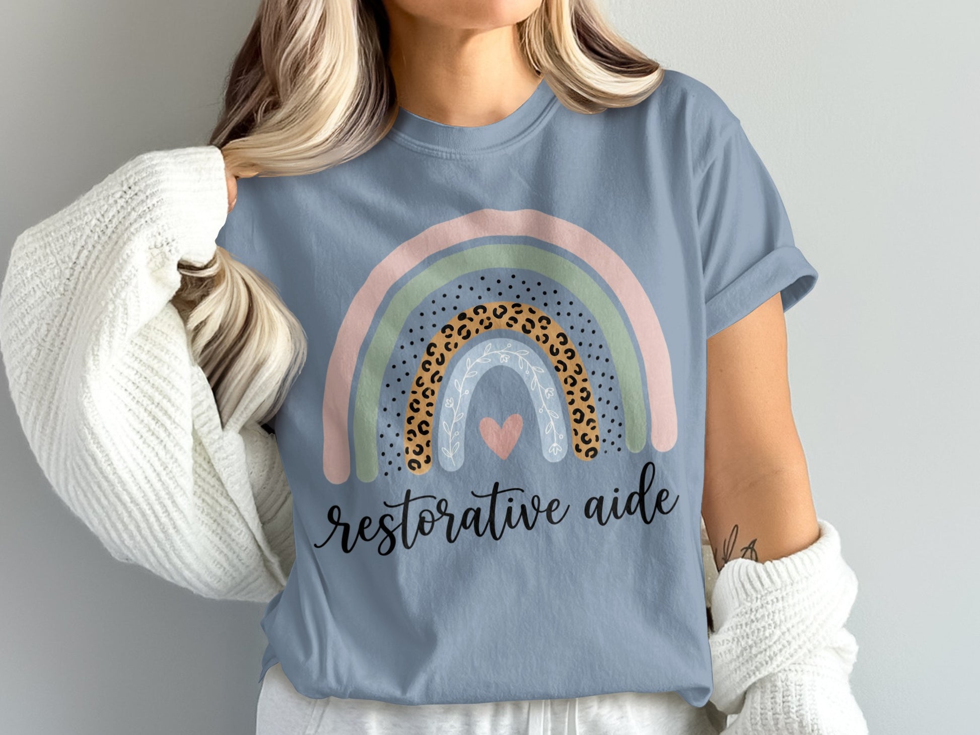 Blue t-shirt with a pastel rainbow, leopard print, heart, and "restorative aide" text.