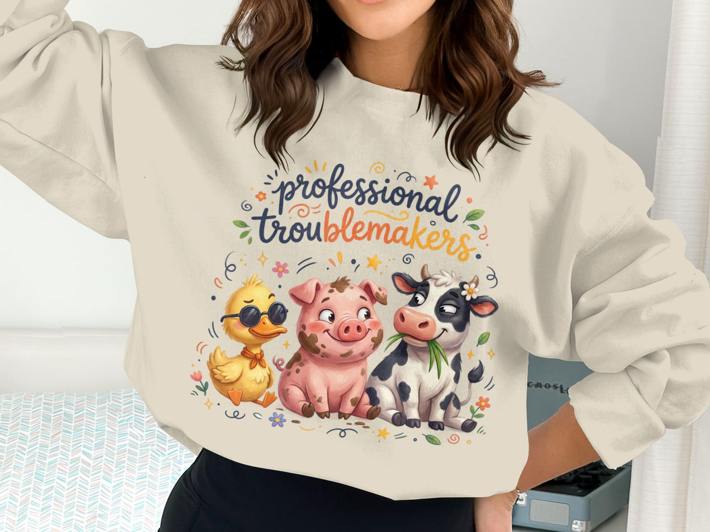 Pig, duck, and cow illustrations on a cream sweatshirt with "professional troublemakers" text.