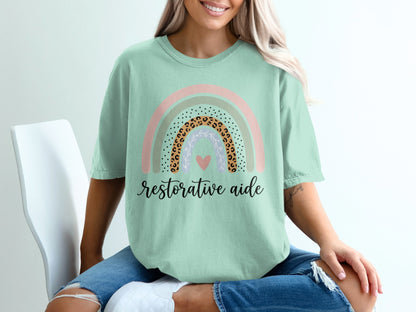 Mint green t-shirt with rainbow graphic and "restorative aide" text.