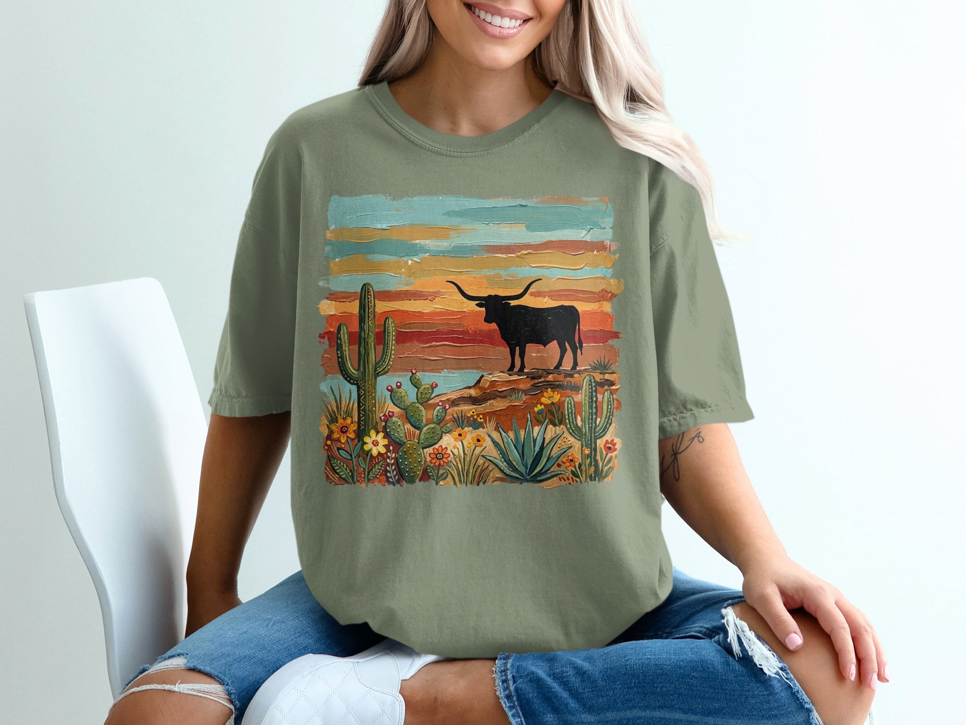 T-shirt with desert landscape: longhorn, cacti, flowers, and colorful sky.