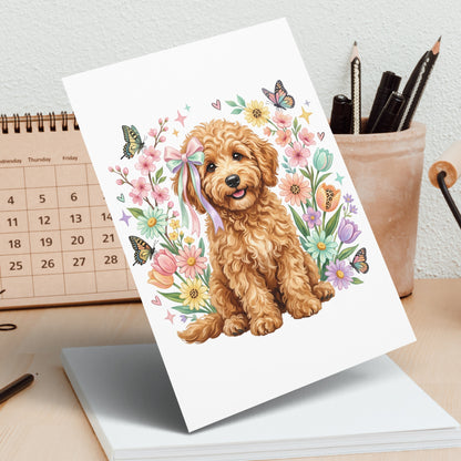 Fluffy goldendoodle puppy with bow sits in floral border with butterflies.