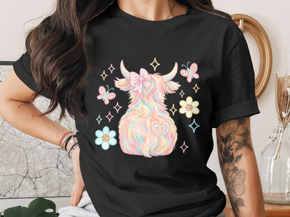 Pastel Highland cow with butterflies, flowers, and heart detail on black t-shirt.