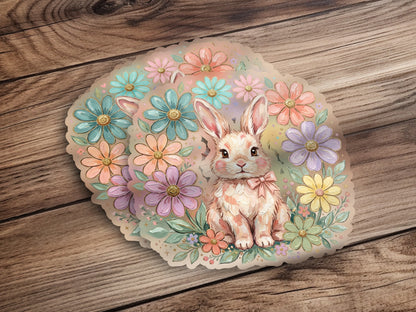 Pink bunny sitting amongst pastel floral arrangement on wooden background.