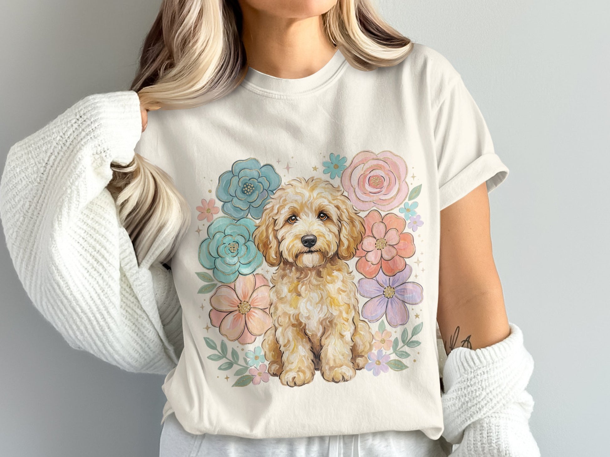 Cream t-shirt with a watercolor-style golden doodle surrounded by pastel flowers.
