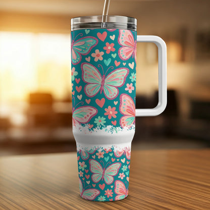 Teal tumbler with pink butterfly and heart pattern, white handle.