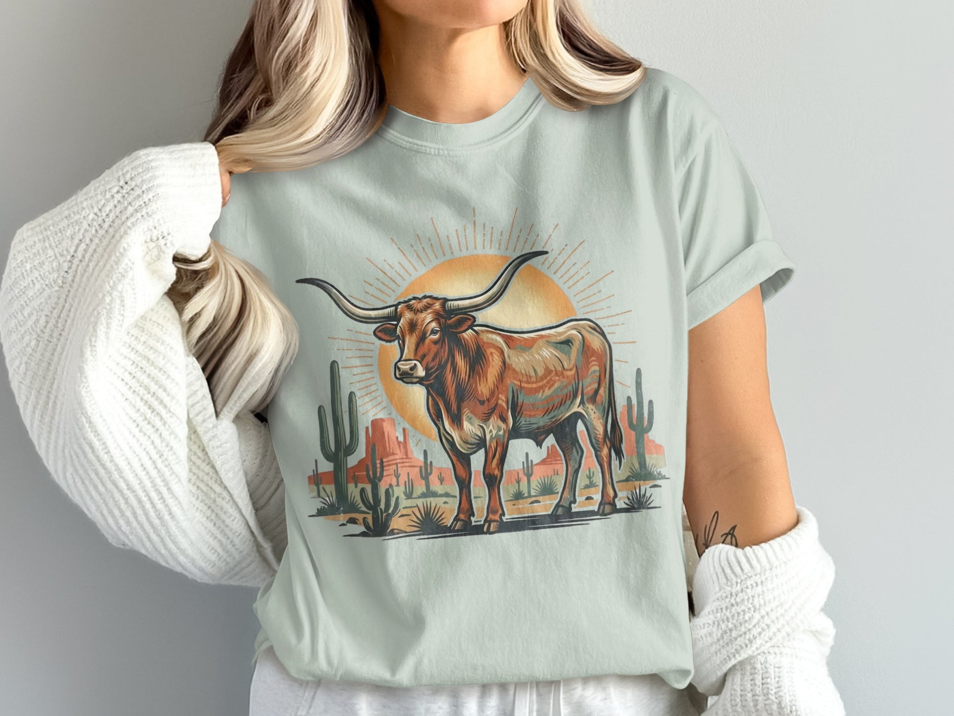 Longhorn steer standing in desert landscape with sun and cacti.