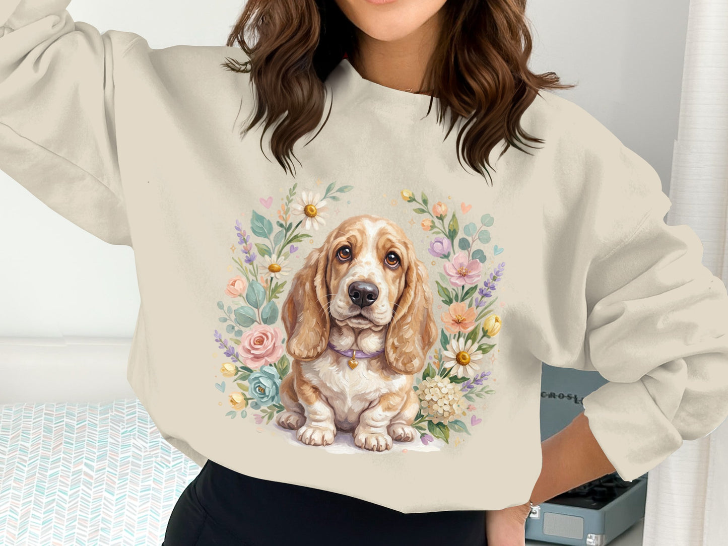 Basset hound puppy surrounded by a floral wreath on a cream sweatshirt.