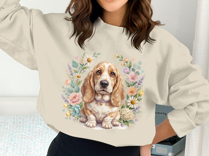 Basset hound puppy surrounded by a floral wreath on a cream sweatshirt.